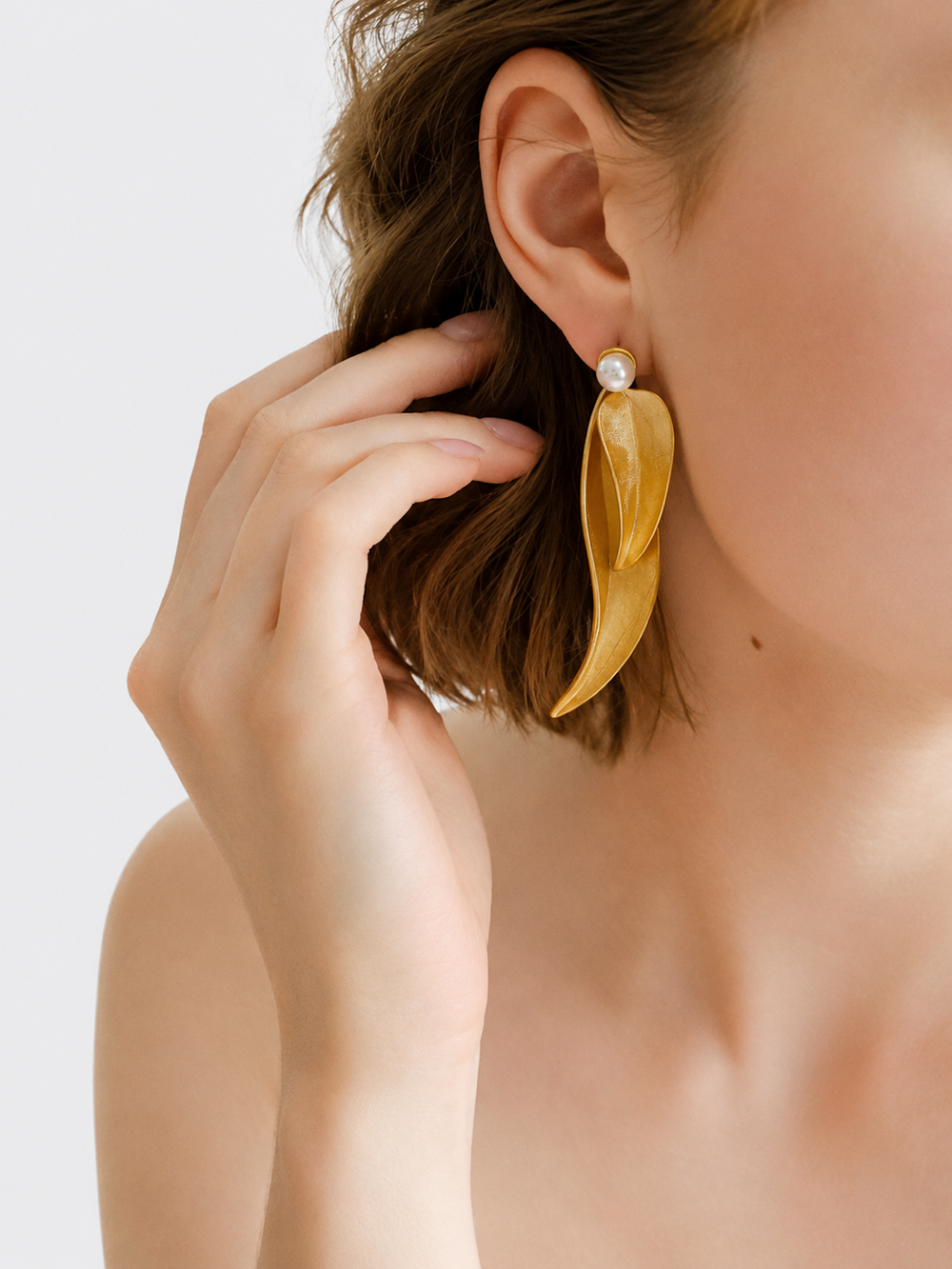 Golden cascading leaf earrings with layered curved leaves and white pearl studs.