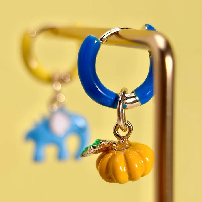 Enchanted Elephant & Pumpkin Enamel Hoop Earrings featuring a blue elephant charm and an orange pumpkin charm with vibrant hand-painted enamel on gold-plated brass hoops, measuring 3 × 1.5 cm.