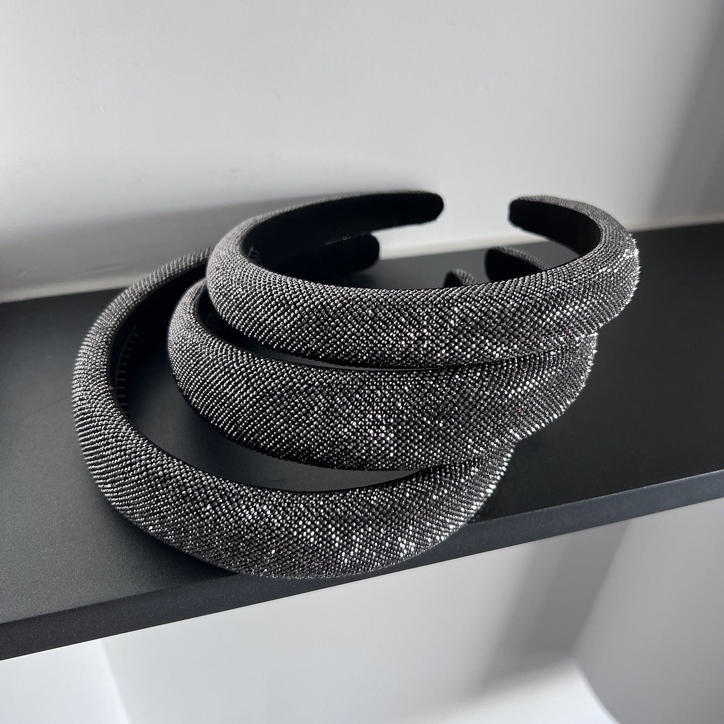 Dark silver pavé crystal padded headband with all-over sparkling embellishments and a sculptural curved silhouette.