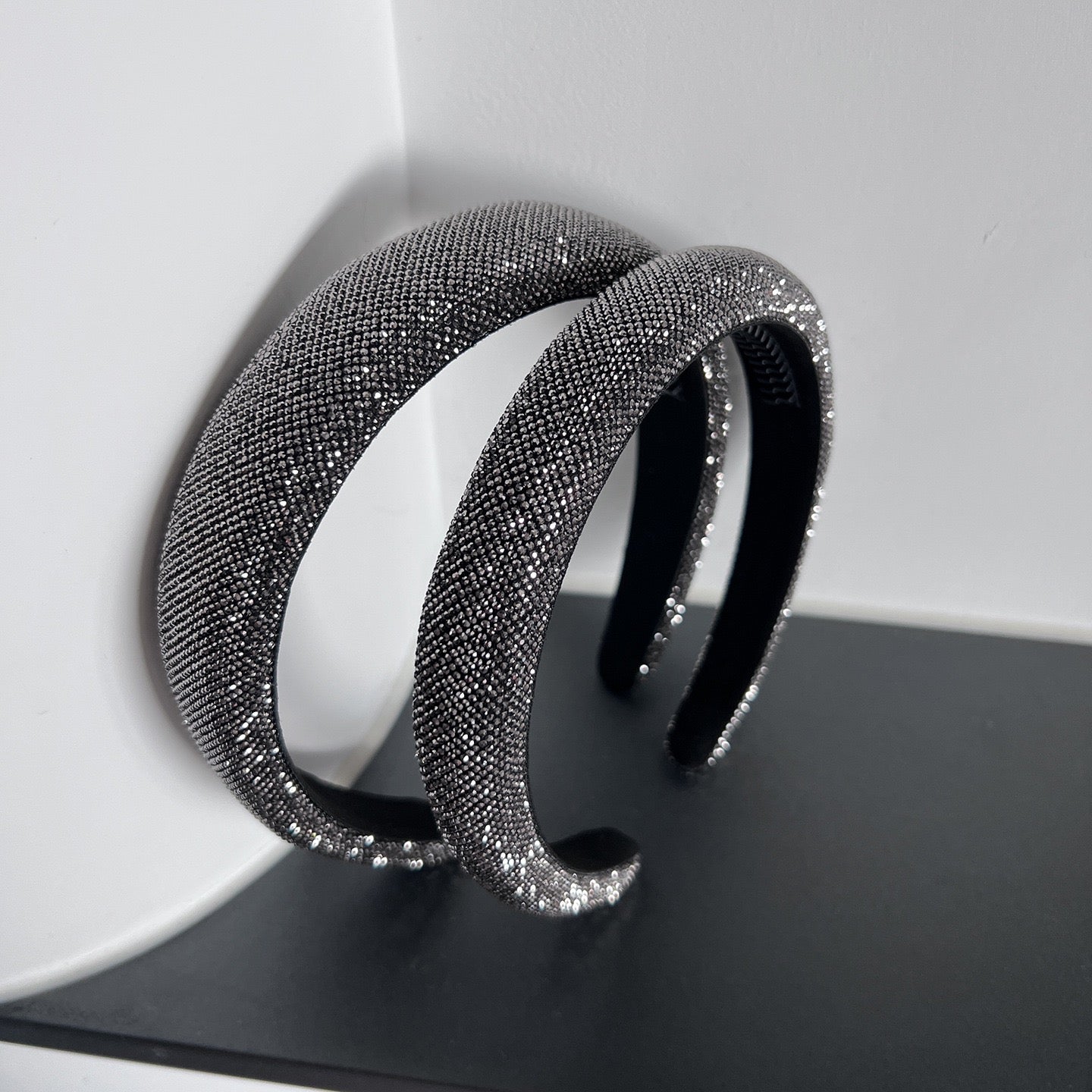 Dark silver pavé crystal padded headband with all-over sparkling embellishments and a sculptural curved silhouette.