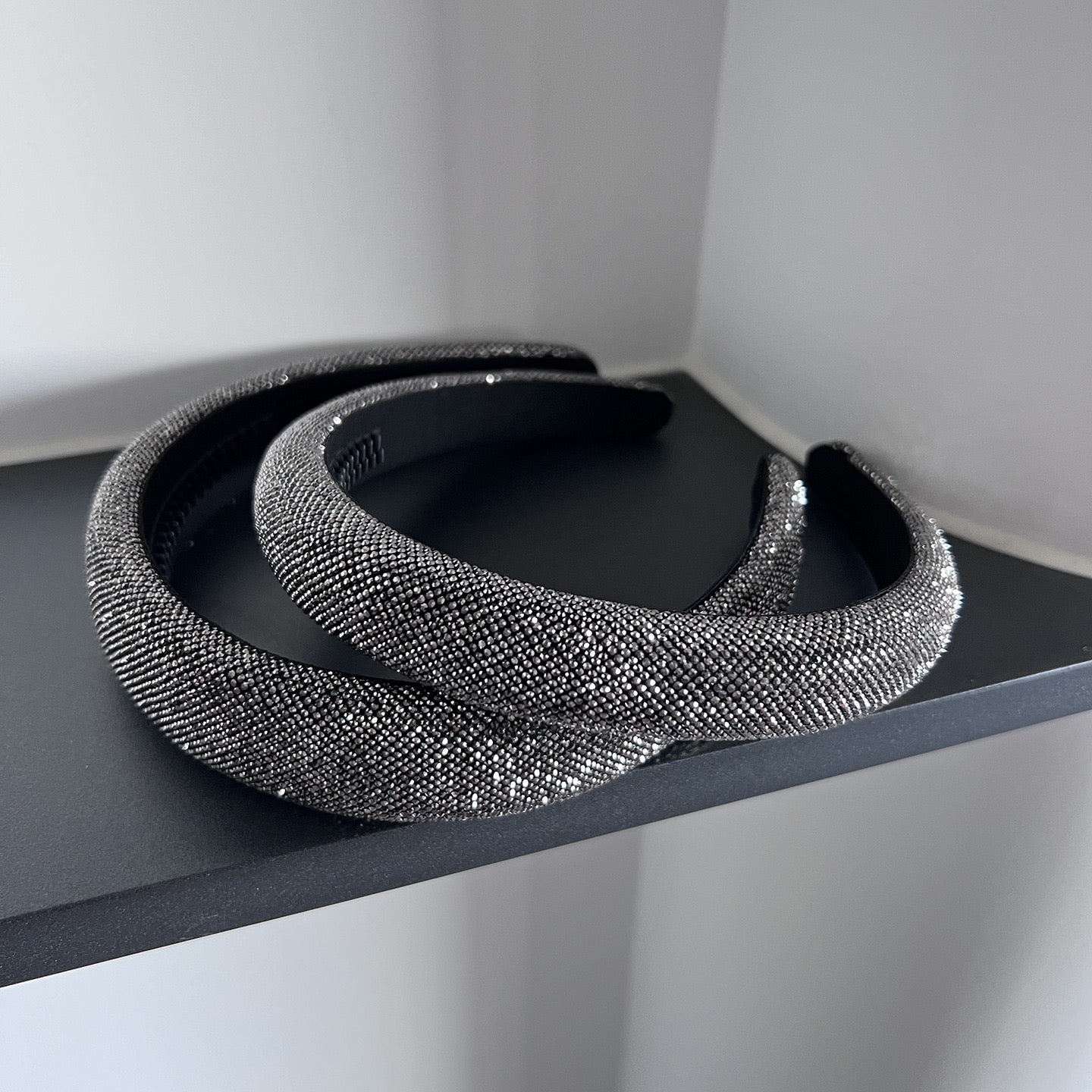 Dark silver pavé crystal padded headband with all-over sparkling embellishments and a sculptural curved silhouette.