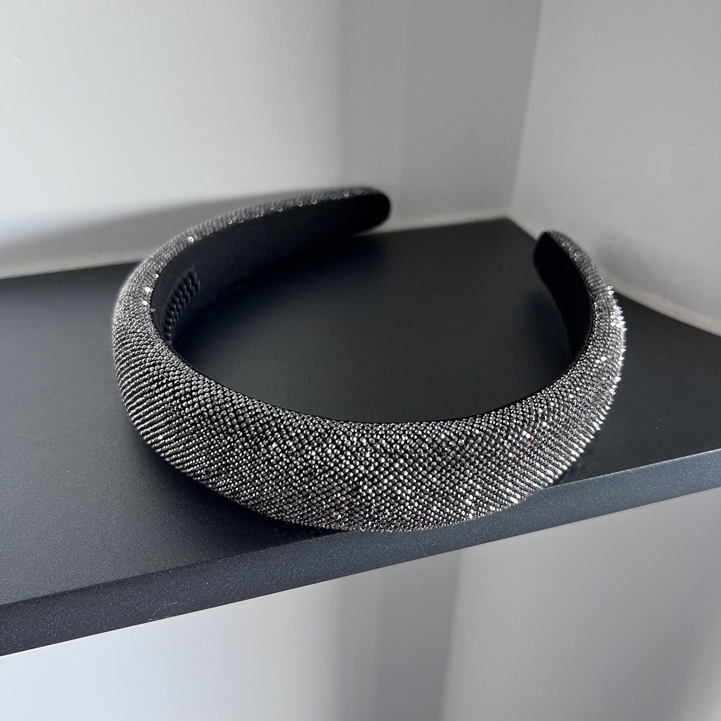 Dark silver pavé crystal padded headband with all-over sparkling embellishments and a sculptural curved silhouette.