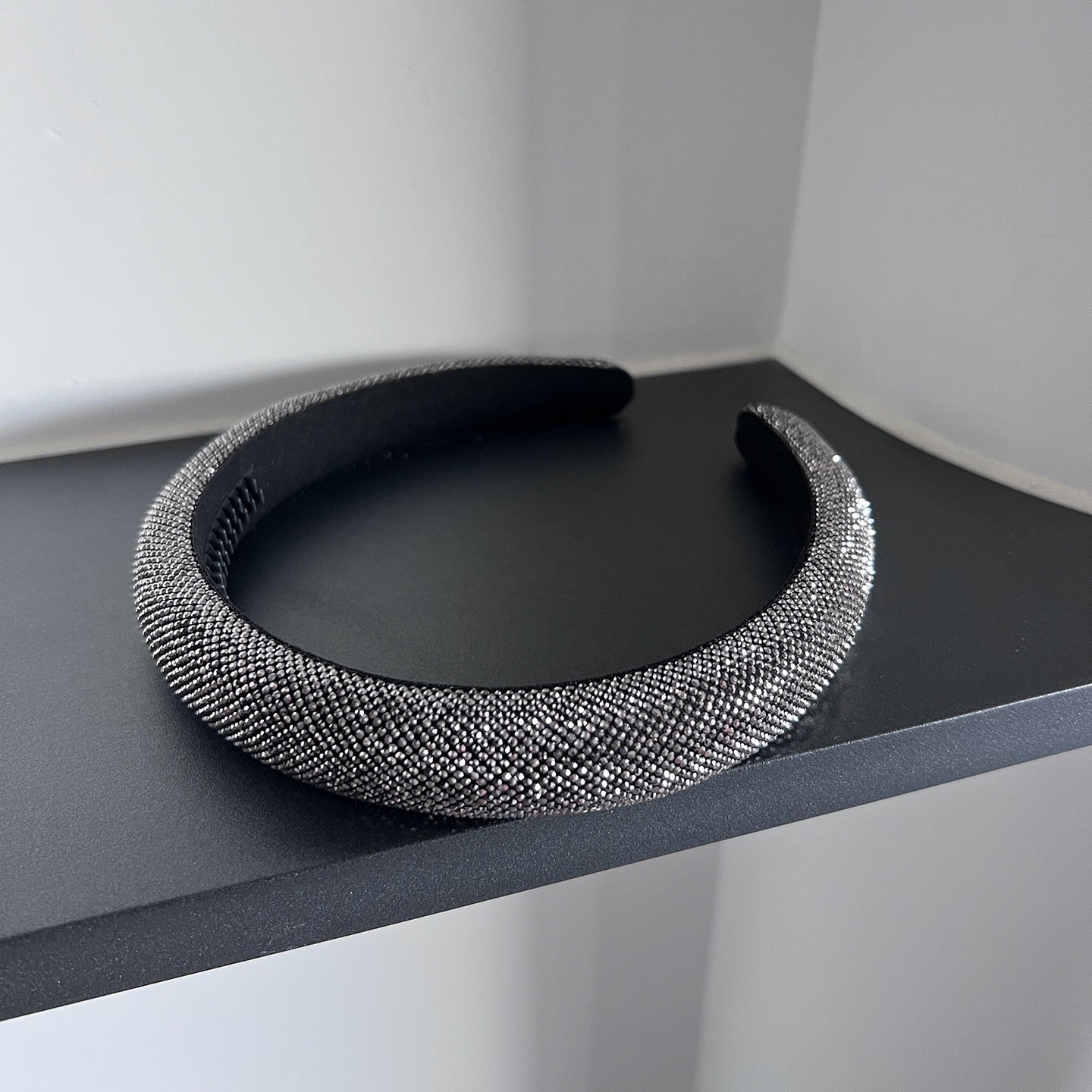 Dark silver pavé crystal padded headband with all-over sparkling embellishments and a sculptural curved silhouette.