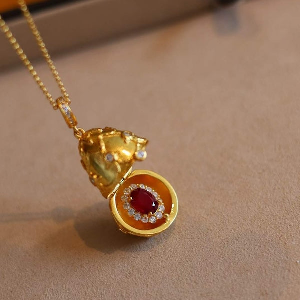 Treasure Egg Locket Ruby Necklace featuring an opening gold-plated egg locket that reveals a genuine ruby surrounded by sparkling zirconia accents.