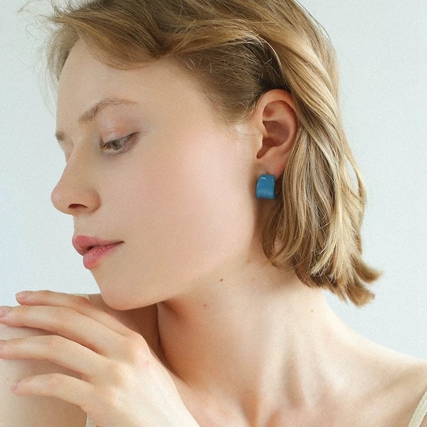 Model wearing cobalt blue enamel hoop earrings crafted from silver-plated brass with a glossy blue enamel finish, alongside a close-up of the minimalist hoop design.