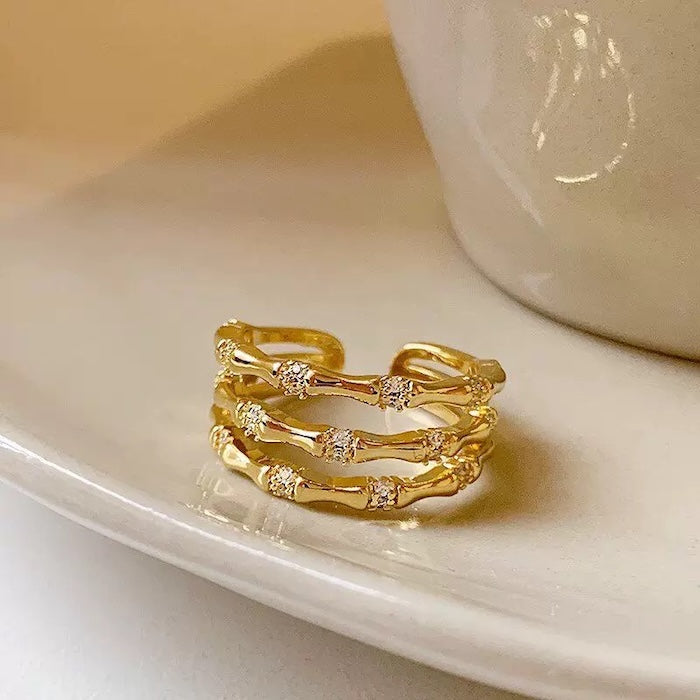 Layered Bamboo Style Adjustable Ring featuring multiple bamboo-inspired gold-tone bands stacked into a bold adjustable ring design.
