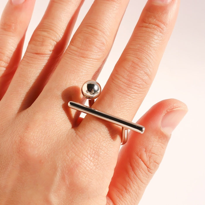Sculptural Beam and Dot Ring featuring a contemporary geometric design with a polished bar and sphere detail, available in gold and silver-tone finishes.
