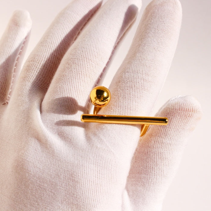 Sculptural Beam and Dot Ring featuring a contemporary geometric design with a polished bar and sphere detail, available in gold and silver-tone finishes.
