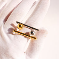 Sculptural Beam and Dot Ring featuring a contemporary geometric design with a polished bar and sphere detail, available in gold and silver-tone finishes.
