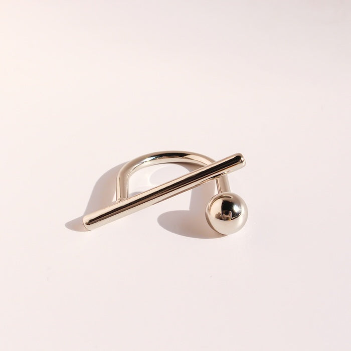 Sculptural Beam and Dot Ring featuring a contemporary geometric design with a polished bar and sphere detail, available in gold and silver-tone finishes.
