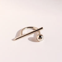 Sculptural Beam and Dot Ring featuring a contemporary geometric design with a polished bar and sphere detail, available in gold and silver-tone finishes.
