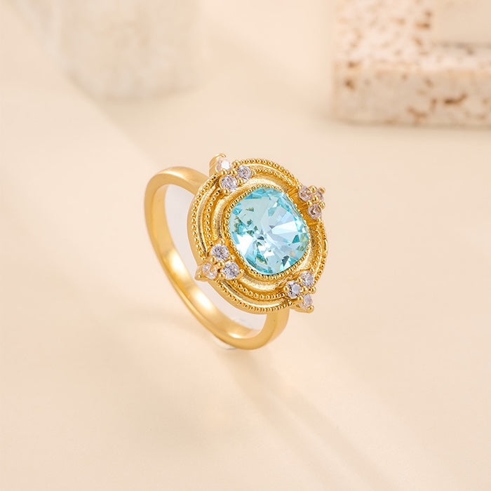 Royal Style Sky Blue Stone Ring featuring a sparkling sky-blue center stone surrounded by zirconia accents in a gold-plated vintage-inspired halo design.
