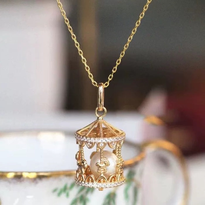 Luxe Carousel Pearl Pendant Necklace featuring a luminous pearl suspended inside an intricately detailed carousel pendant with sparkling accents and a gold-tone finish on a 40 + 5 cm chain.