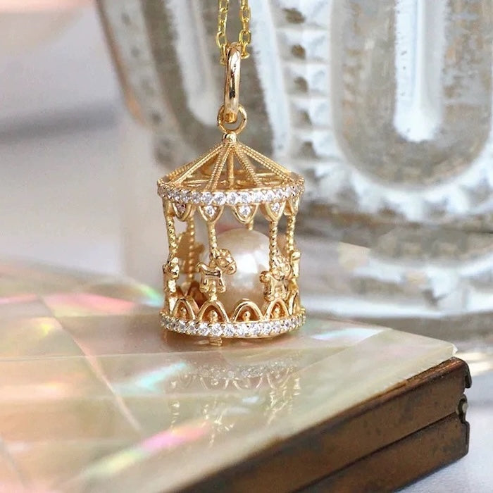 Luxe Carousel Pearl Pendant Necklace featuring a luminous pearl suspended inside an intricately detailed carousel pendant with sparkling accents and a gold-tone finish on a 40 + 5 cm chain.
