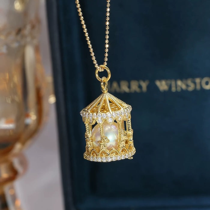 Luxe Carousel Pearl Pendant Necklace featuring a luminous pearl suspended inside an intricately detailed carousel pendant with sparkling accents and a gold-tone finish on a 40 + 5 cm chain.