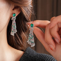 Emerald Ribbon Cascade Earrings with an emerald green teardrop crystal, silver-plated finish, sparkling zirconia, ribbon-inspired detailing, and crystal tassels.
