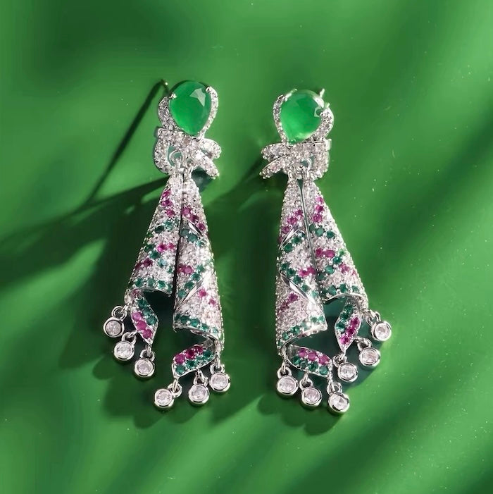 Emerald Ribbon Cascade Earrings with an emerald green teardrop crystal, silver-plated finish, sparkling zirconia, ribbon-inspired detailing, and crystal tassels.