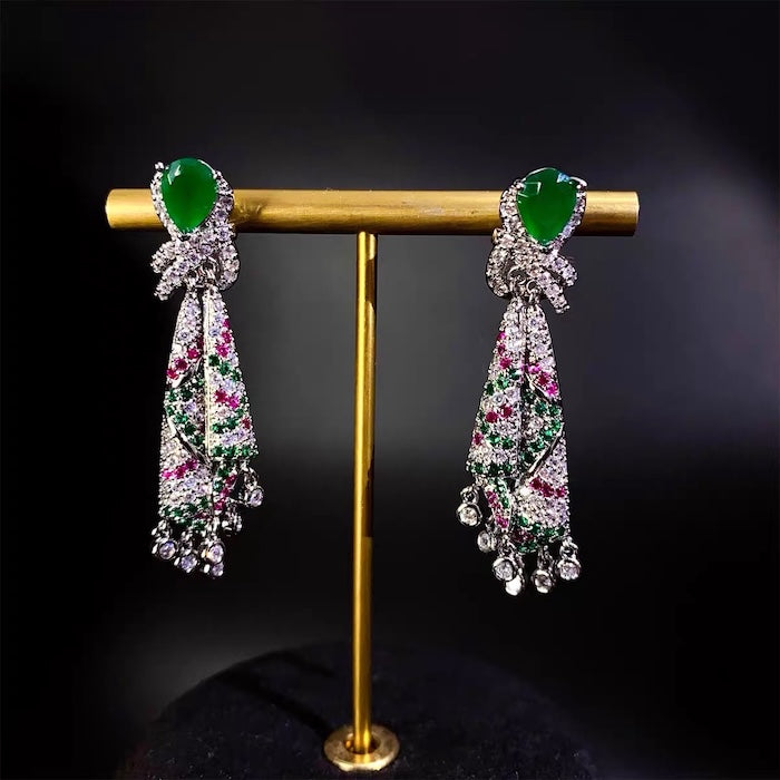 Emerald Ribbon Cascade Earrings with an emerald green teardrop crystal, silver-plated finish, sparkling zirconia, ribbon-inspired detailing, and crystal tassels.