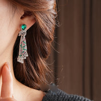 Emerald Ribbon Cascade Earrings with an emerald green teardrop crystal, silver-plated finish, sparkling zirconia, ribbon-inspired detailing, and crystal tassels.