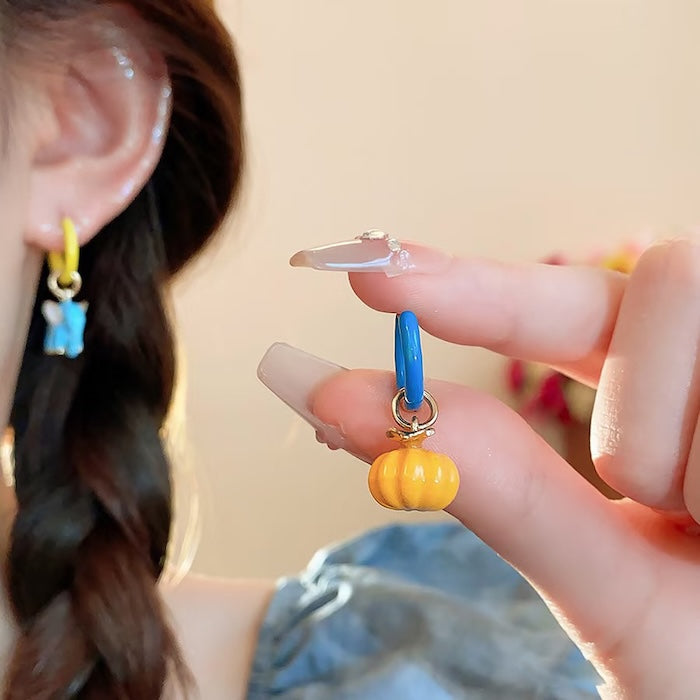 Enchanted Elephant & Pumpkin Enamel Hoop Earrings featuring a blue elephant charm and an orange pumpkin charm with vibrant hand-painted enamel on gold-plated brass hoops, measuring 3 × 1.5 cm.
