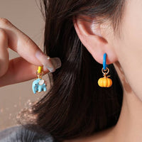 Enchanted Elephant & Pumpkin Enamel Hoop Earrings featuring a blue elephant charm and an orange pumpkin charm with vibrant hand-painted enamel on gold-plated brass hoops, measuring 3 × 1.5 cm.