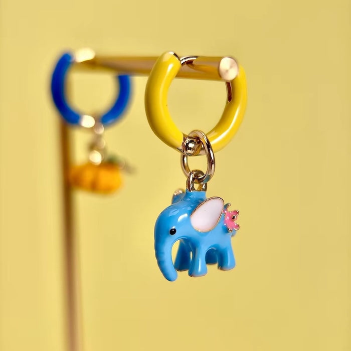 Enchanted Elephant & Pumpkin Enamel Hoop Earrings featuring a blue elephant charm and an orange pumpkin charm with vibrant hand-painted enamel on gold-plated brass hoops, measuring 3 × 1.5 cm.