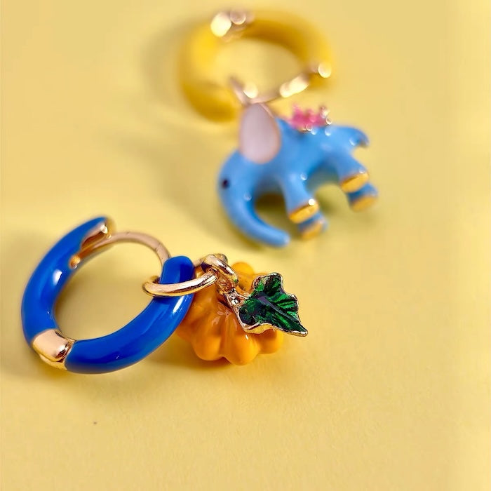 Enchanted Elephant & Pumpkin Enamel Hoop Earrings featuring a blue elephant charm and an orange pumpkin charm with vibrant hand-painted enamel on gold-plated brass hoops, measuring 3 × 1.5 cm.