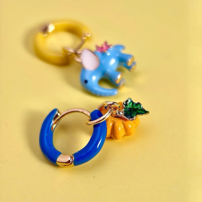 Enchanted Elephant & Pumpkin Enamel Hoop Earrings featuring a blue elephant charm and an orange pumpkin charm with vibrant hand-painted enamel on gold-plated brass hoops, measuring 3 × 1.5 cm.