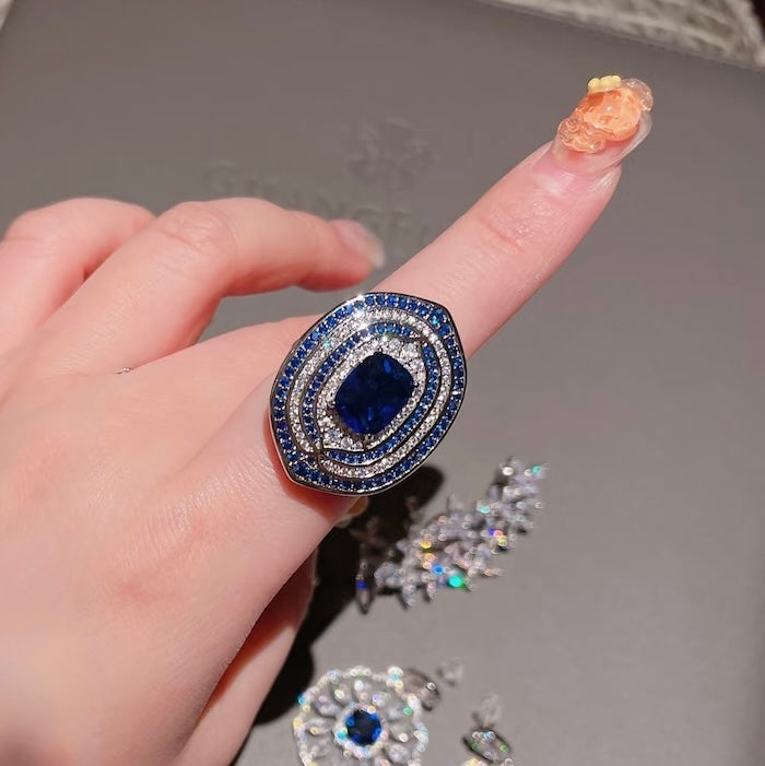 Royal Sapphire Halo Crystal Dress Ring in white gold-plated brass featuring a sapphire-blue center crystal with layered blue and clear crystal halos.
