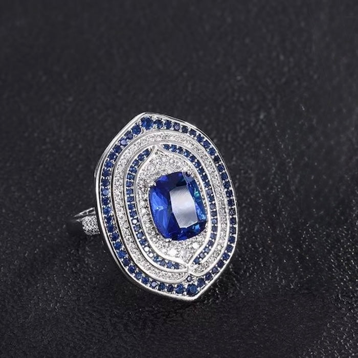 Royal Sapphire Halo Crystal Dress Ring in white gold-plated brass featuring a sapphire-blue center crystal with layered blue and clear crystal halos.
