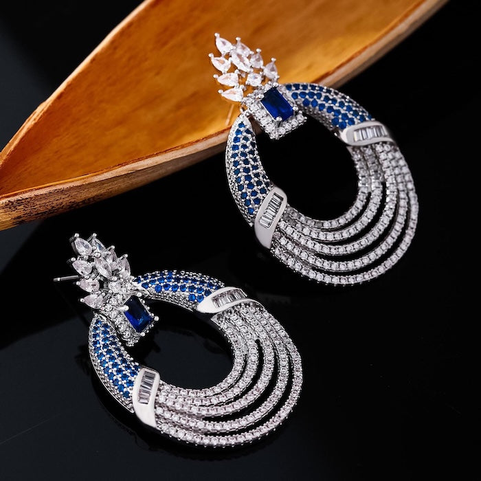 Royal Style Sapphire Look Oversized Earrings featuring sapphire-blue zirconias, sparkling pavé crystal details, and an elegant silver-tone statement design.
