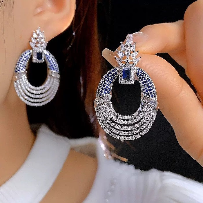 Royal Style Sapphire Look Oversized Earrings featuring sapphire-blue zirconias, sparkling pavé crystal details, and an elegant silver-tone statement design.
