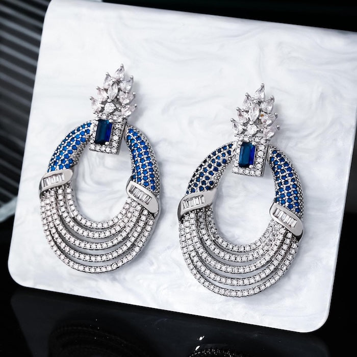Royal Style Sapphire Look Oversized Earrings featuring sapphire-blue zirconias, sparkling pavé crystal details, and an elegant silver-tone statement design.
