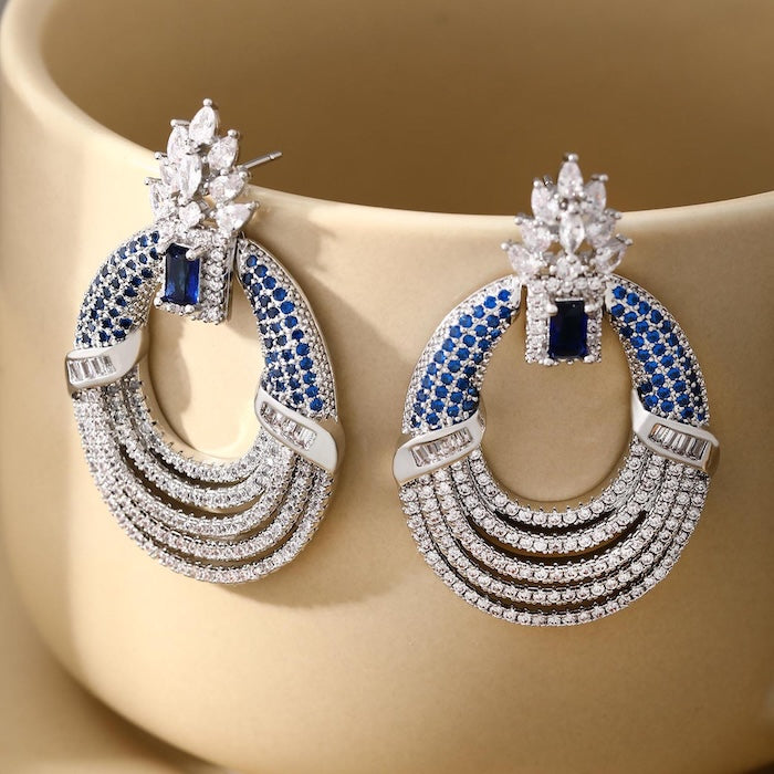 Royal Style Sapphire Look Oversized Earrings featuring sapphire-blue zirconias, sparkling pavé crystal details, and an elegant silver-tone statement design.
