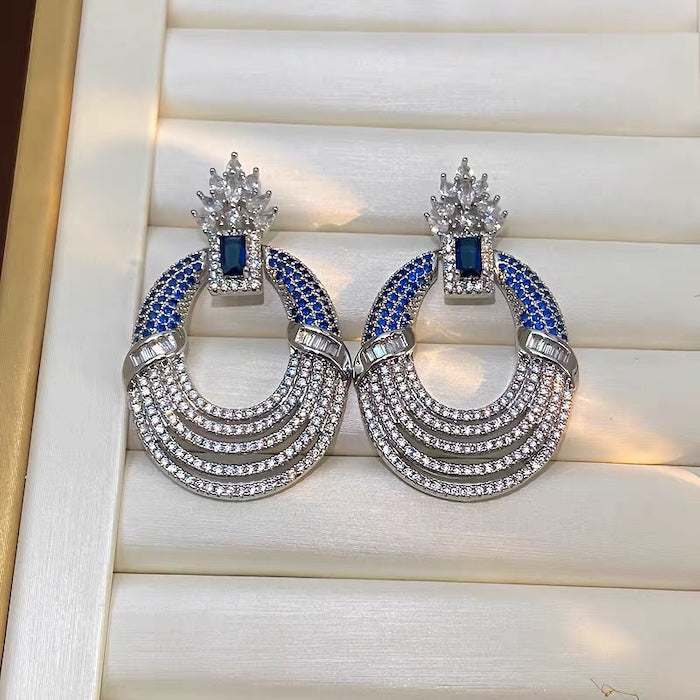 Royal Style Sapphire Look Oversized Earrings featuring sapphire-blue zirconias, sparkling pavé crystal details, and an elegant silver-tone statement design.

