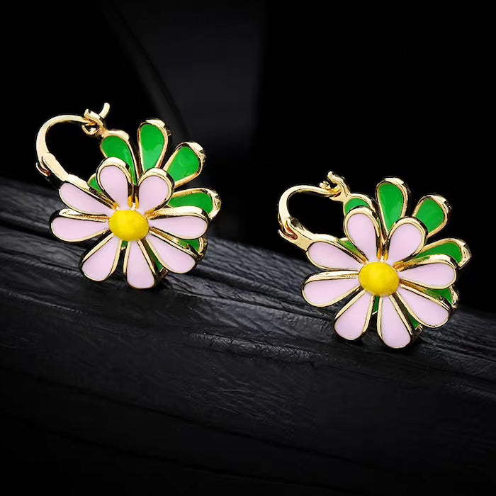 Golden Twin Daisy Hoop Earrings featuring one green enamel daisy and one soft pink enamel daisy suspended from polished gold-tone hoops.