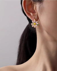 Golden Twin Daisy Hoop Earrings featuring one green enamel daisy and one soft pink enamel daisy suspended from polished gold-tone hoops.