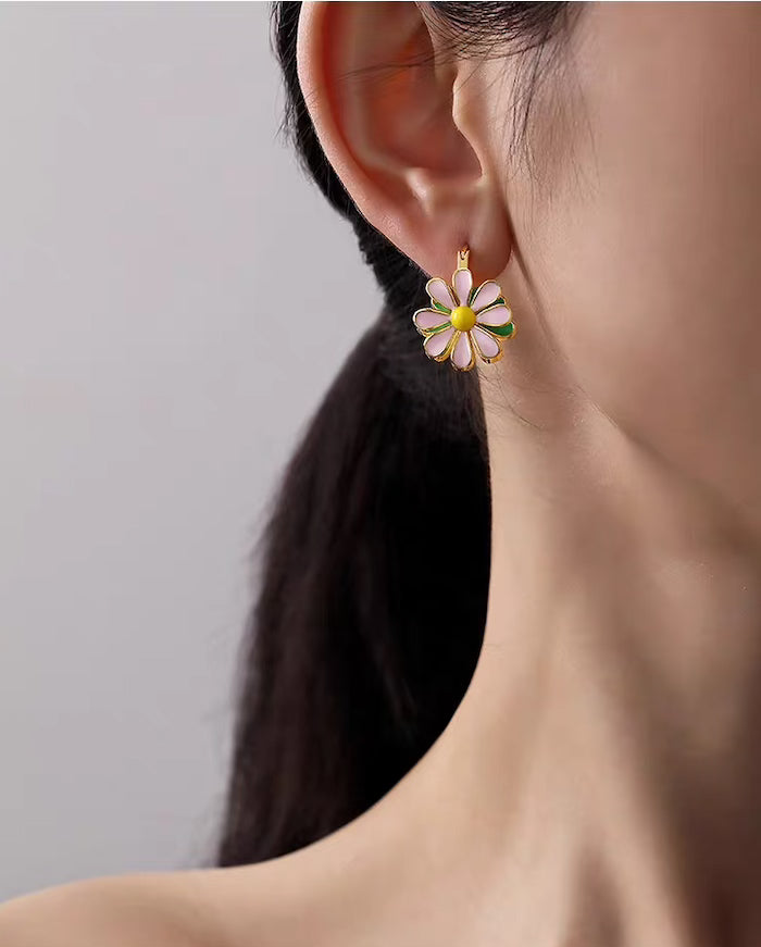 Golden Twin Daisy Hoop Earrings featuring one green enamel daisy and one soft pink enamel daisy suspended from polished gold-tone hoops.