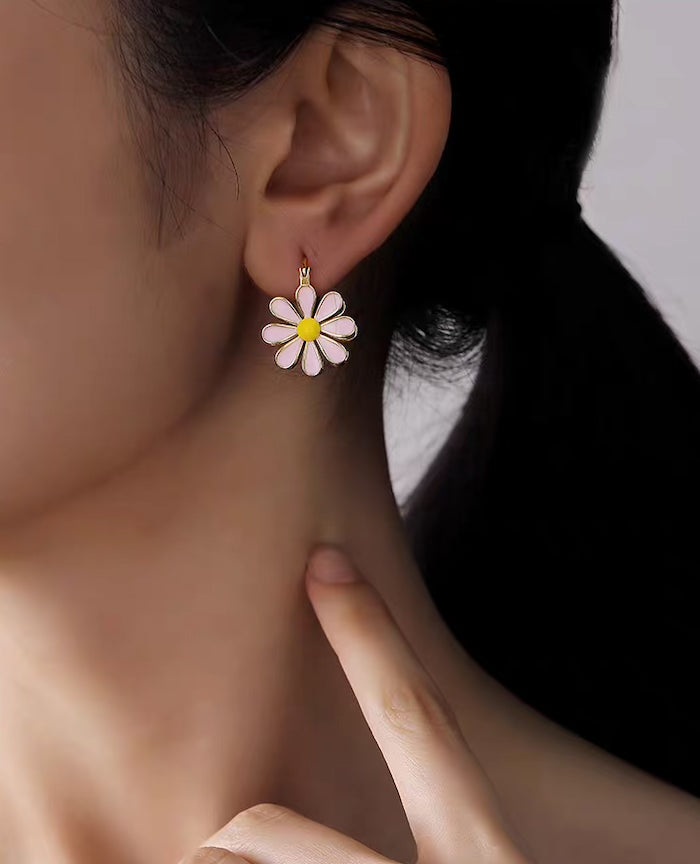  Golden Twin Daisy Hoop Earrings featuring one green enamel daisy and one soft pink enamel daisy suspended from polished gold-tone hoops.