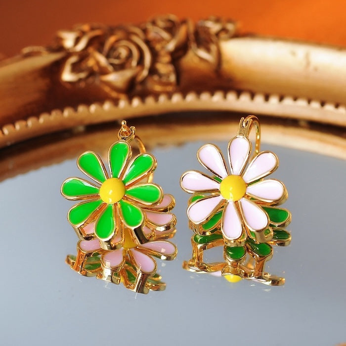Golden Twin Daisy Hoop Earrings featuring one green enamel daisy and one soft pink enamel daisy suspended from polished gold-tone hoops.
