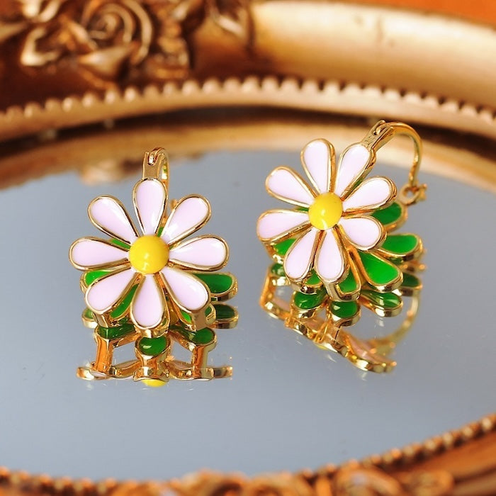 Golden Twin Daisy Hoop Earrings featuring one green enamel daisy and one soft pink enamel daisy suspended from polished gold-tone hoops.