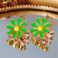 Golden Twin Daisy Hoop Earrings featuring one green enamel daisy and one soft pink enamel daisy suspended from polished gold-tone hoops.