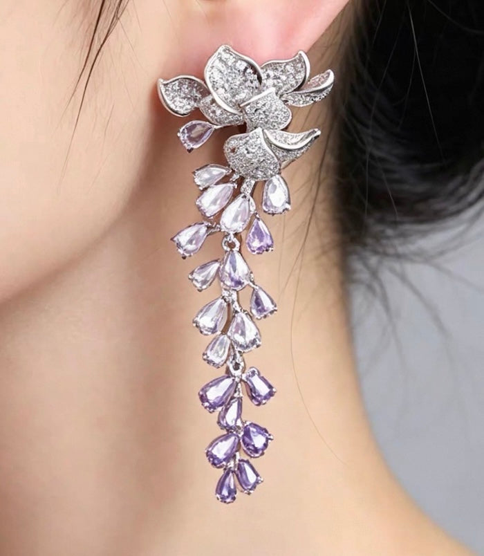 Dazzling Wisteria Flower Tassel Earrings featuring sparkling floral zirconia details and cascading lavender-toned crystal tassels in a silver-tone setting.
