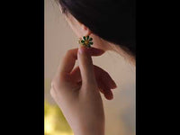 Golden Twin Daisy Hoop Earrings featuring one green enamel daisy and one soft pink enamel daisy suspended from polished gold-tone hoops.